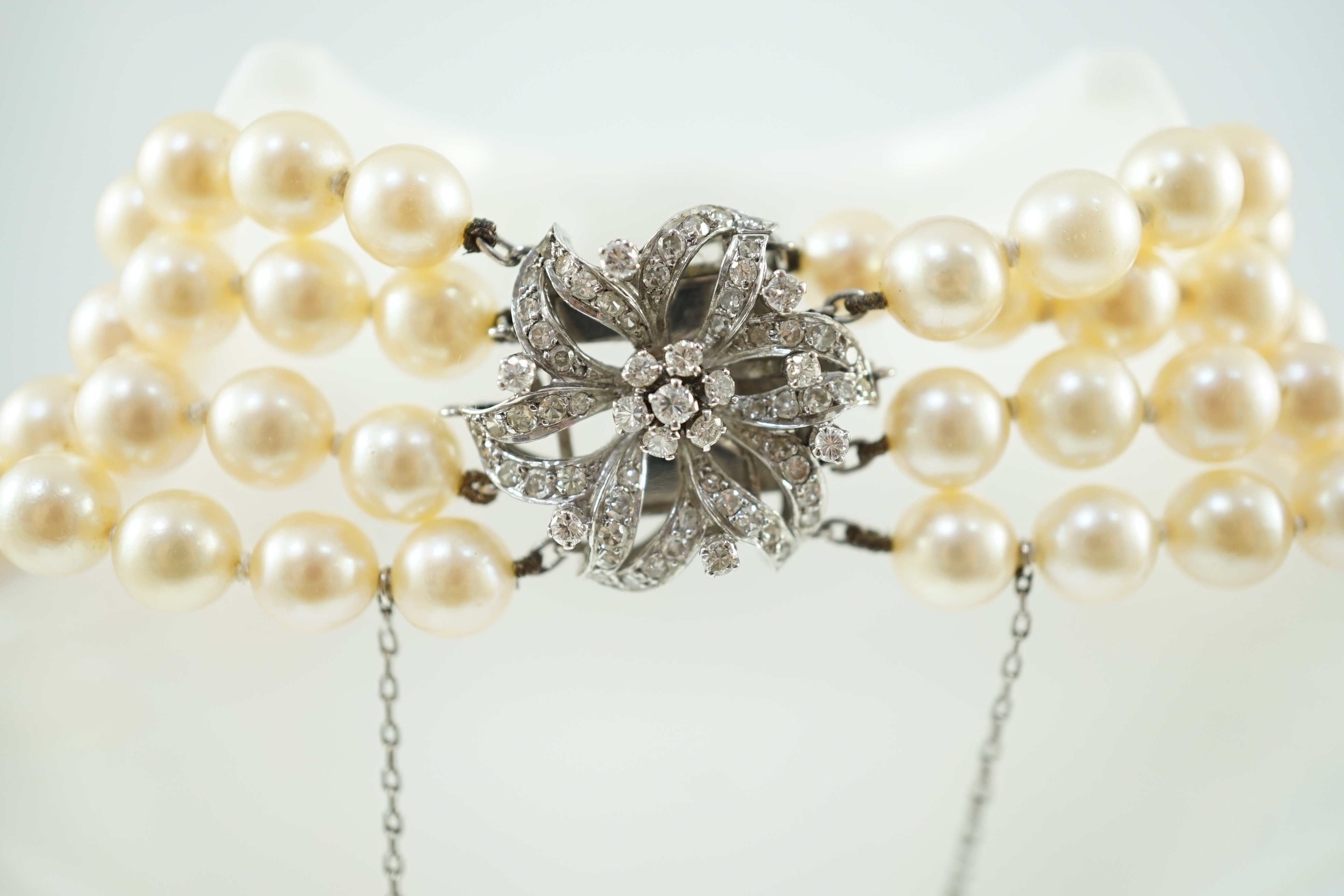 A mid to late 20th century continental quadruple strand cultured pearl necklace, with white gold and diamond cluster set flower head clasp